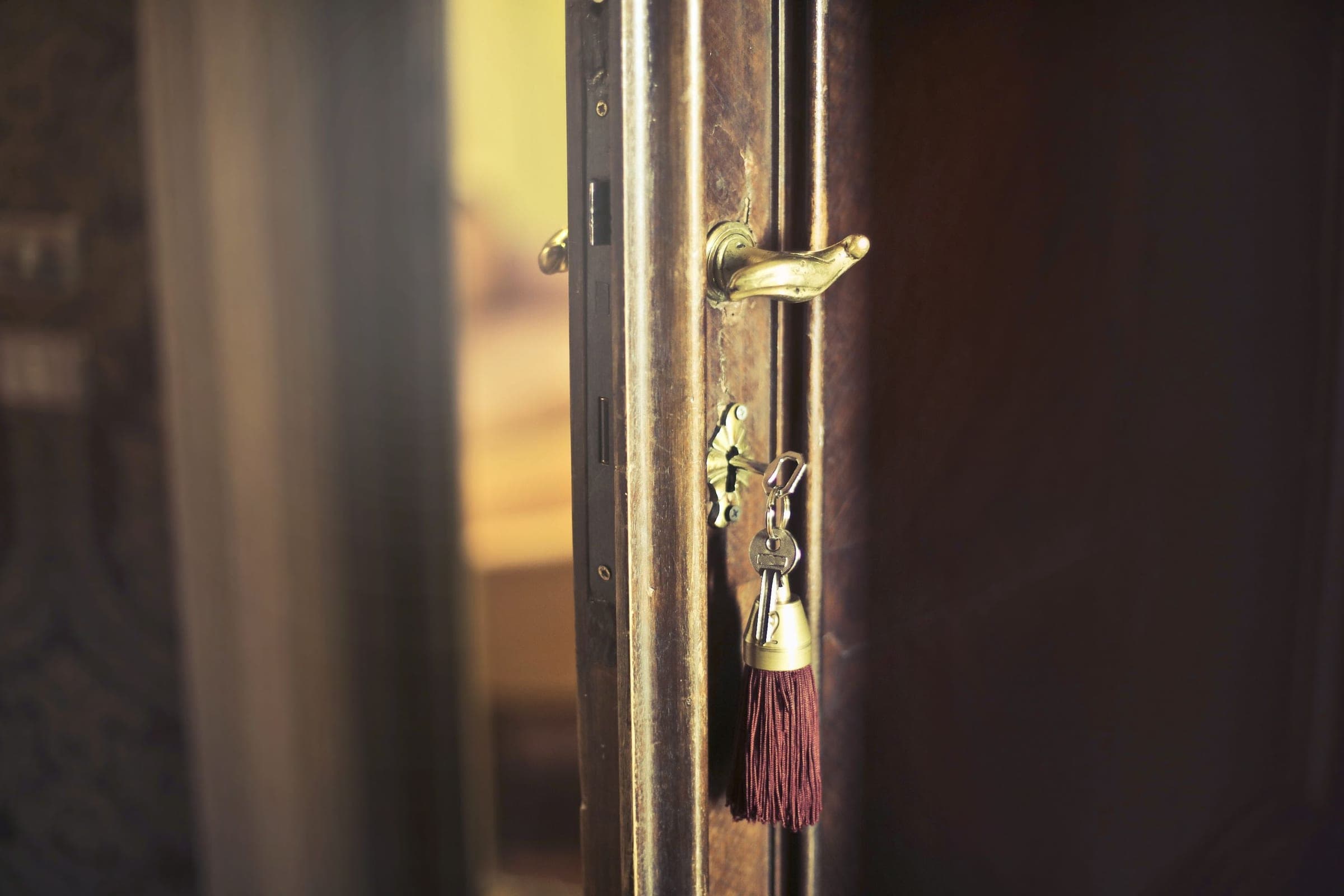 A brass room key with a tasselled fob, hanging in an old door's lock.