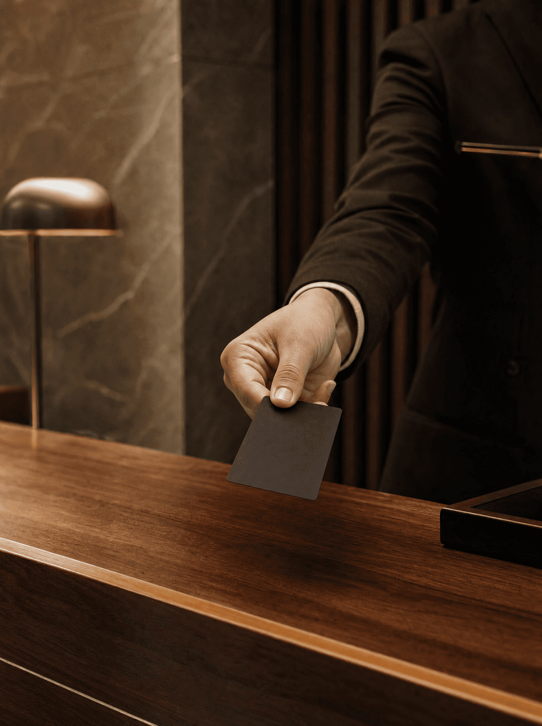 A hand offering a plain dark credential card across a hotel reception desk.