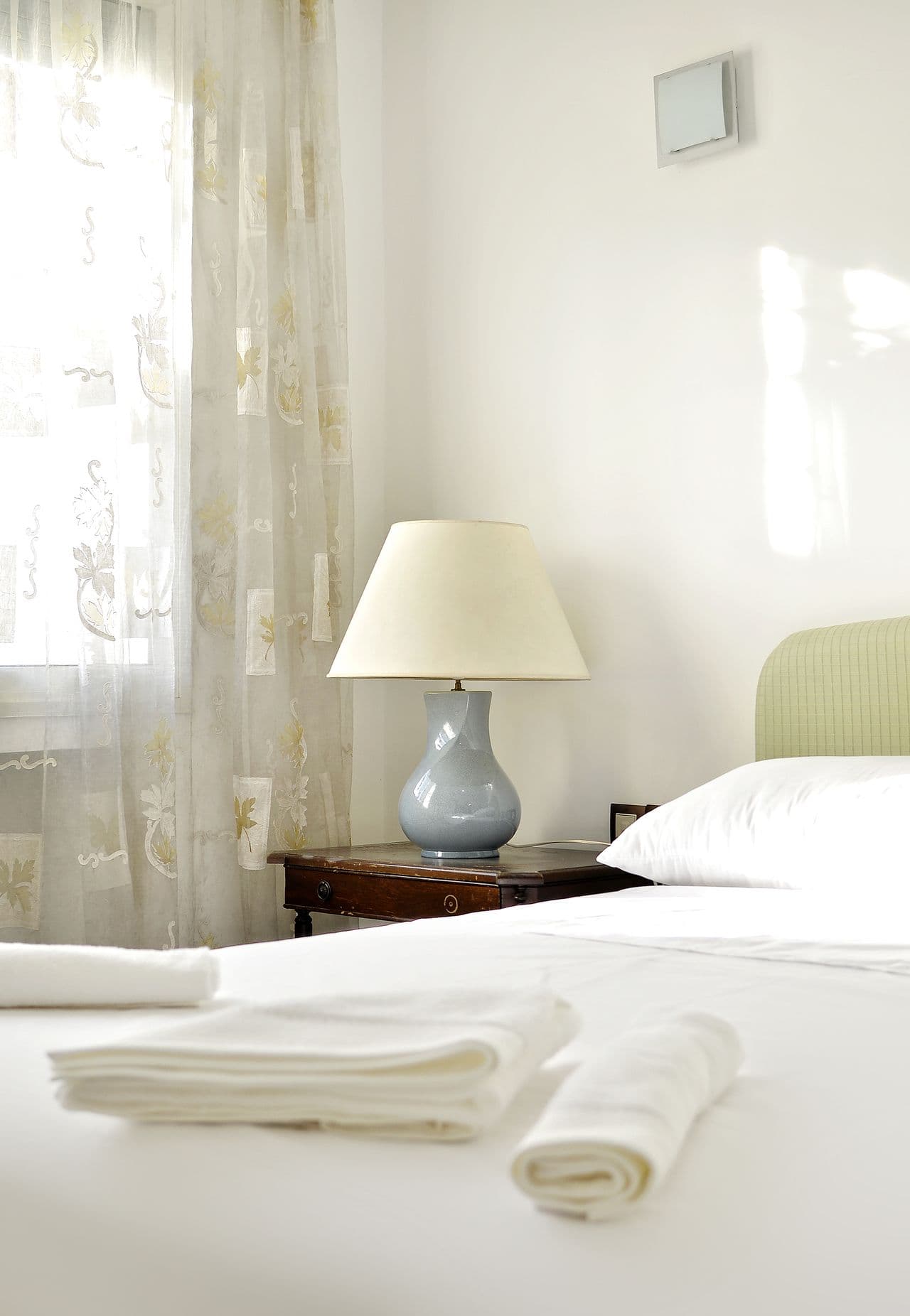Folded white towels resting on a crisply made hotel bed, morning light through sheer curtains.