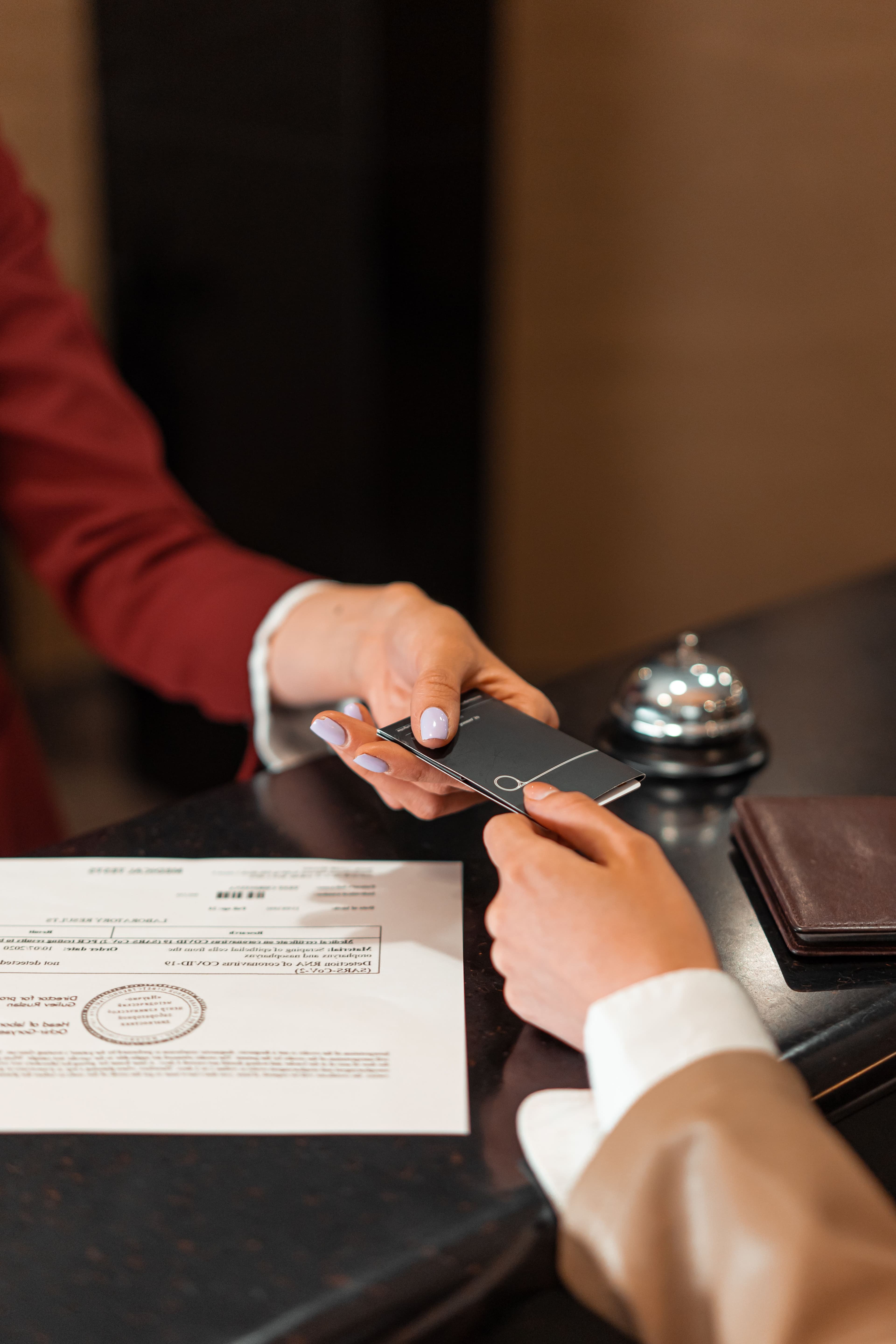 Two hands exchanging a room key card across a hotel reception desk.