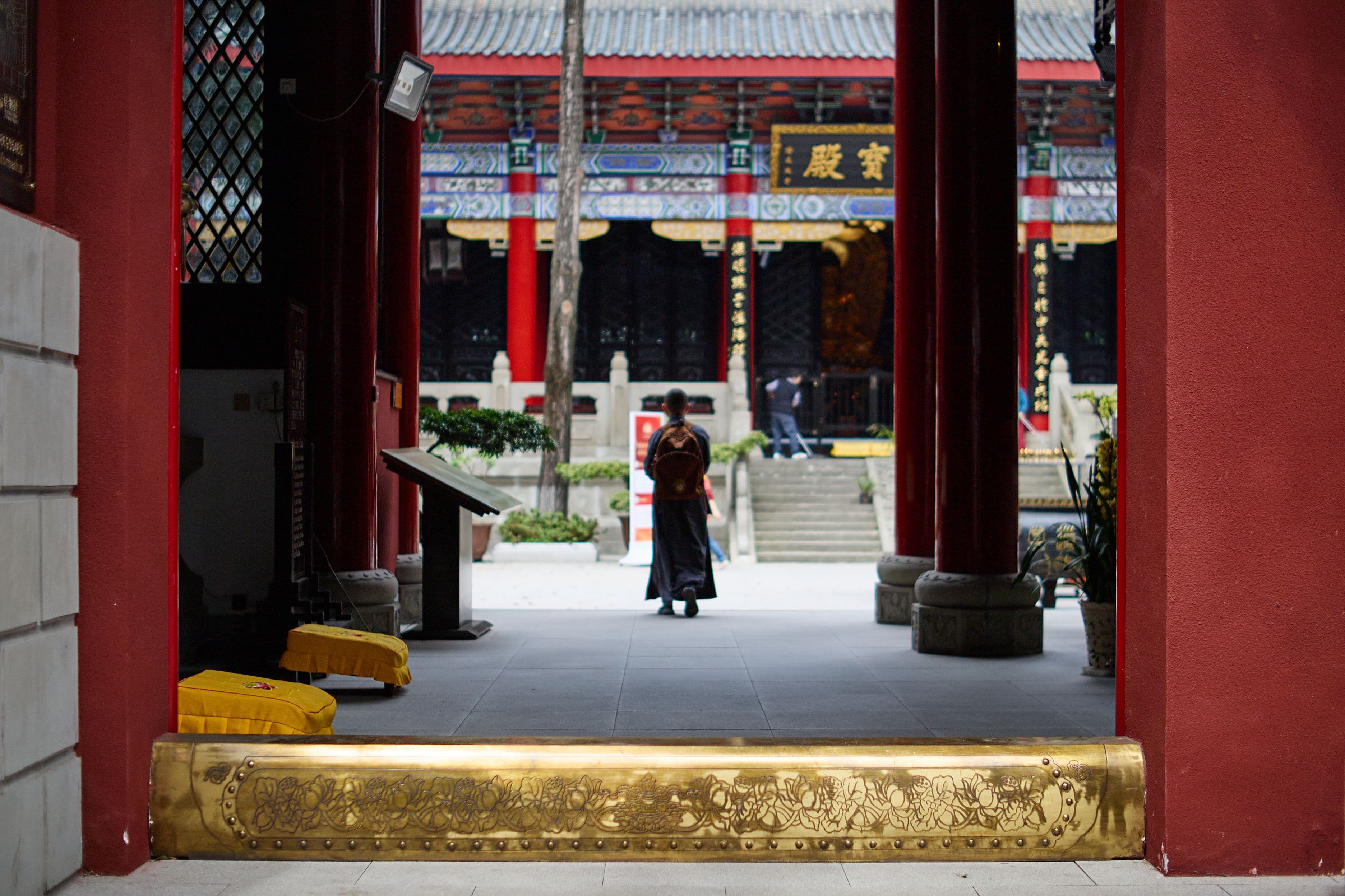 A temple’s red-columned entrance hall, a robed monk walking through the courtyard beyond.