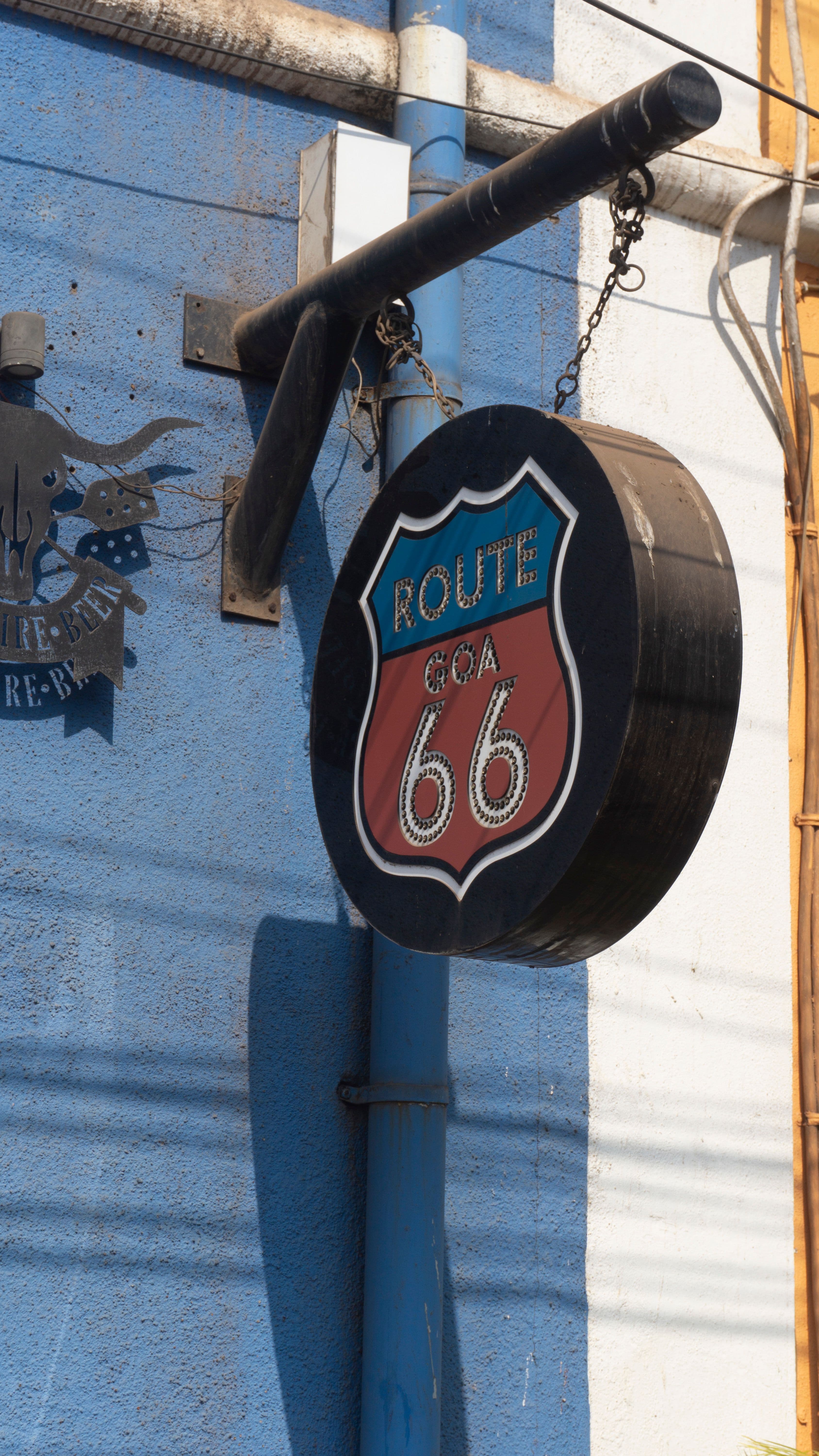 A round shop sign reading "Route Goa 66" mounted on a blue building wall.
