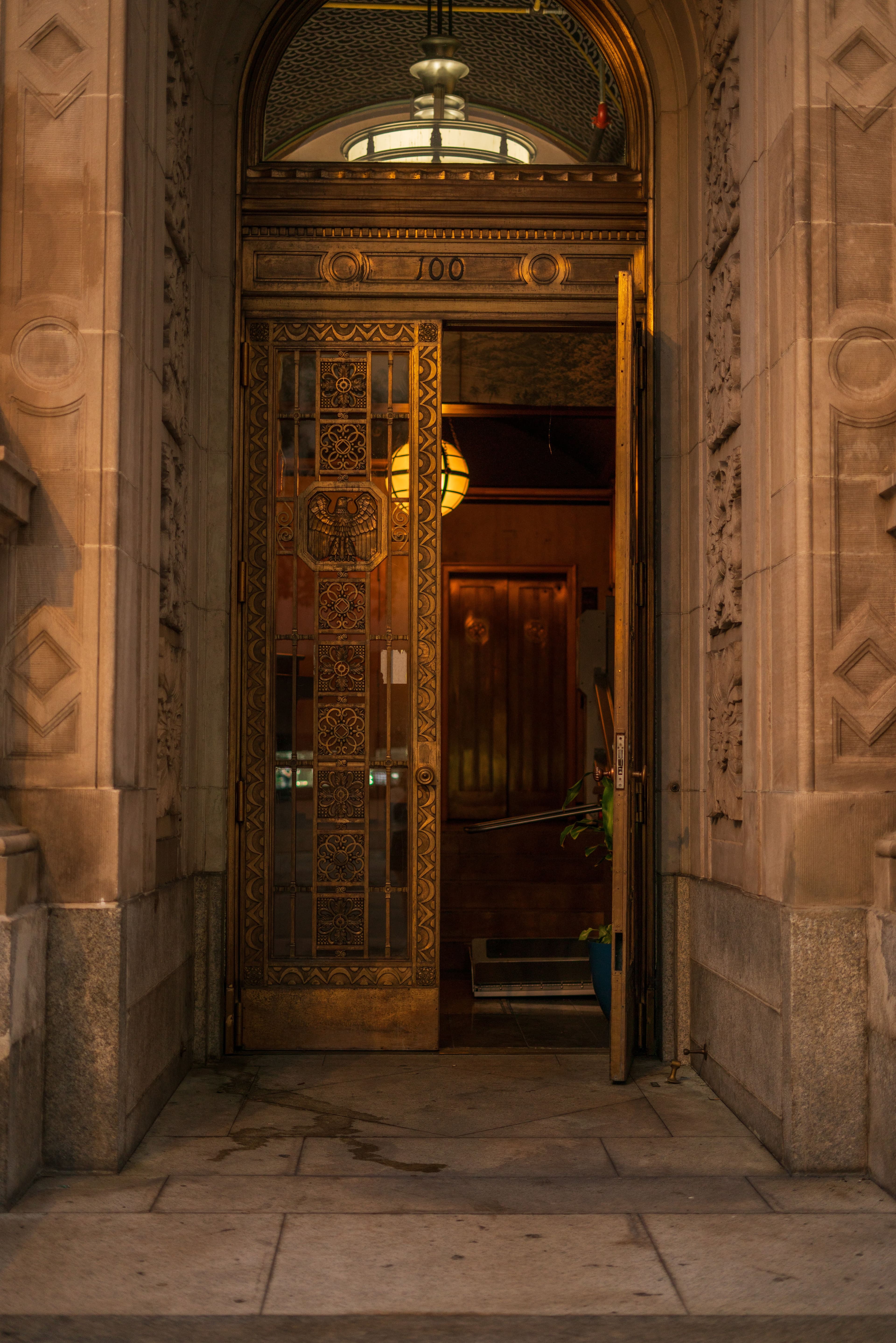An ornate brass-trimmed door standing open onto a warm-lit lobby.