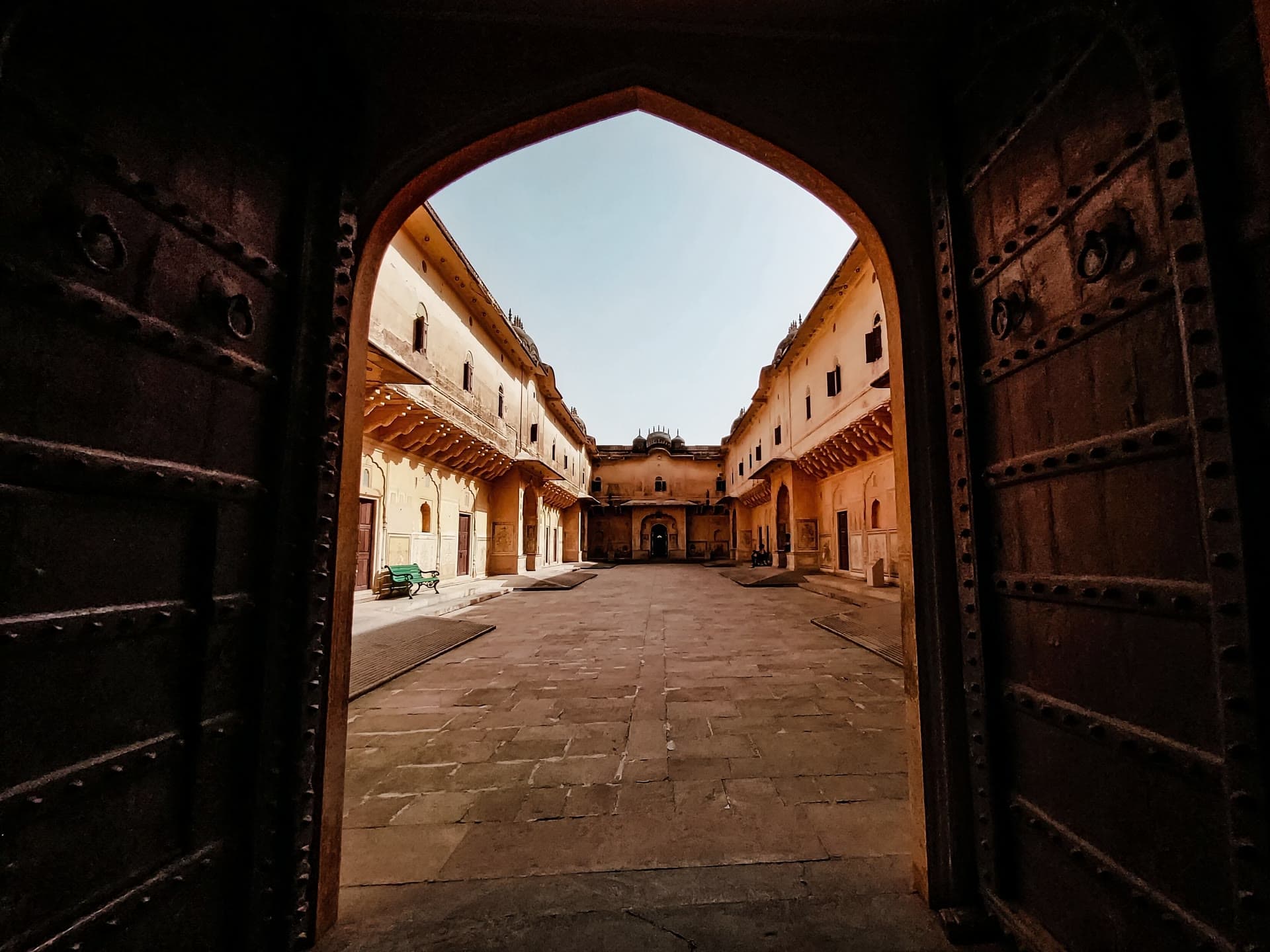 Iron-studded gates standing open onto a sunlit heritage courtyard.